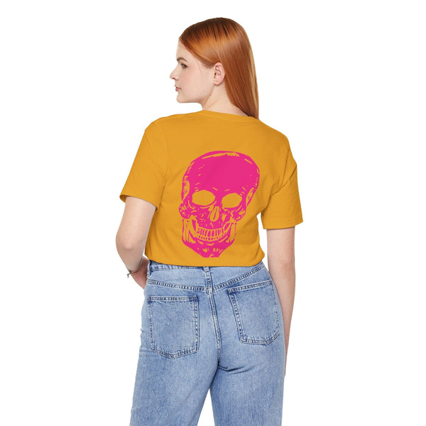 Woman wearing a mustard yellow punk rock tee with a bold pink skull graphic on the back, paired with light blue jeans.