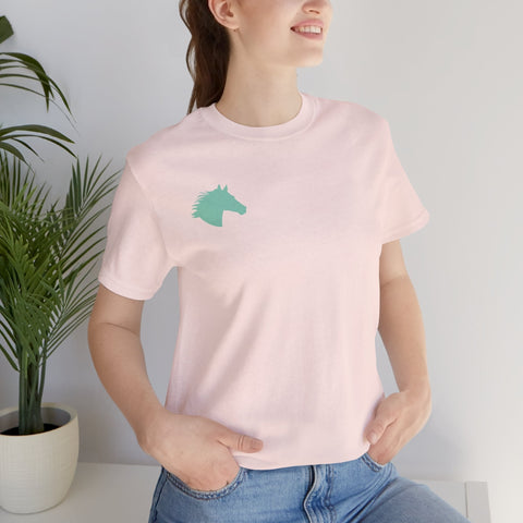 Woman wearing light pink t shirt with minimalist aqua horse head print on left chest standing indoors by a plant